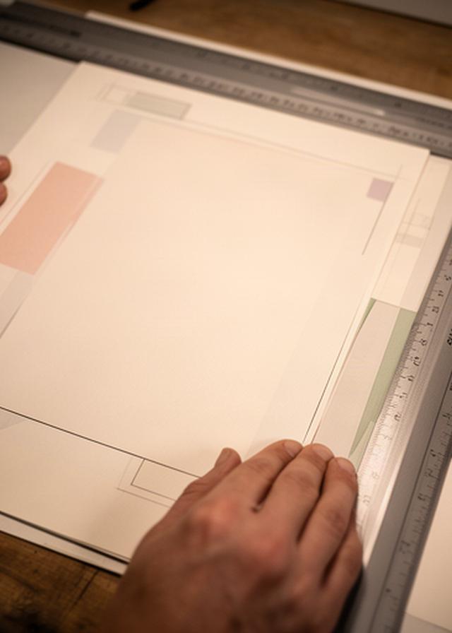 Close view of hands reviewing a printed proof with measured margins on a workshop table